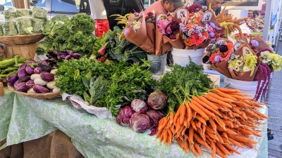 Peak season market display of greens, roots, fruits and flowers.
